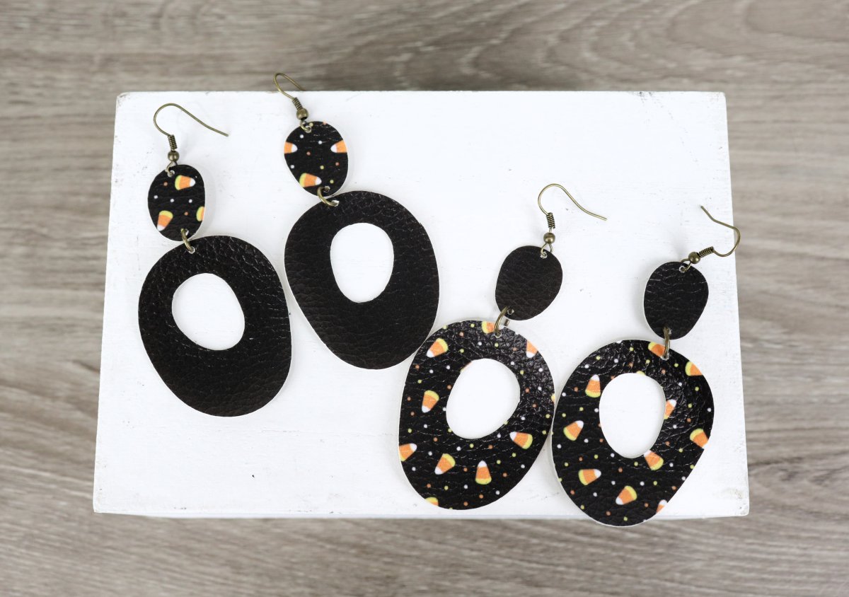 Image contains two pair of dangle earrings made from black and black/candy corn patterned faux leather.