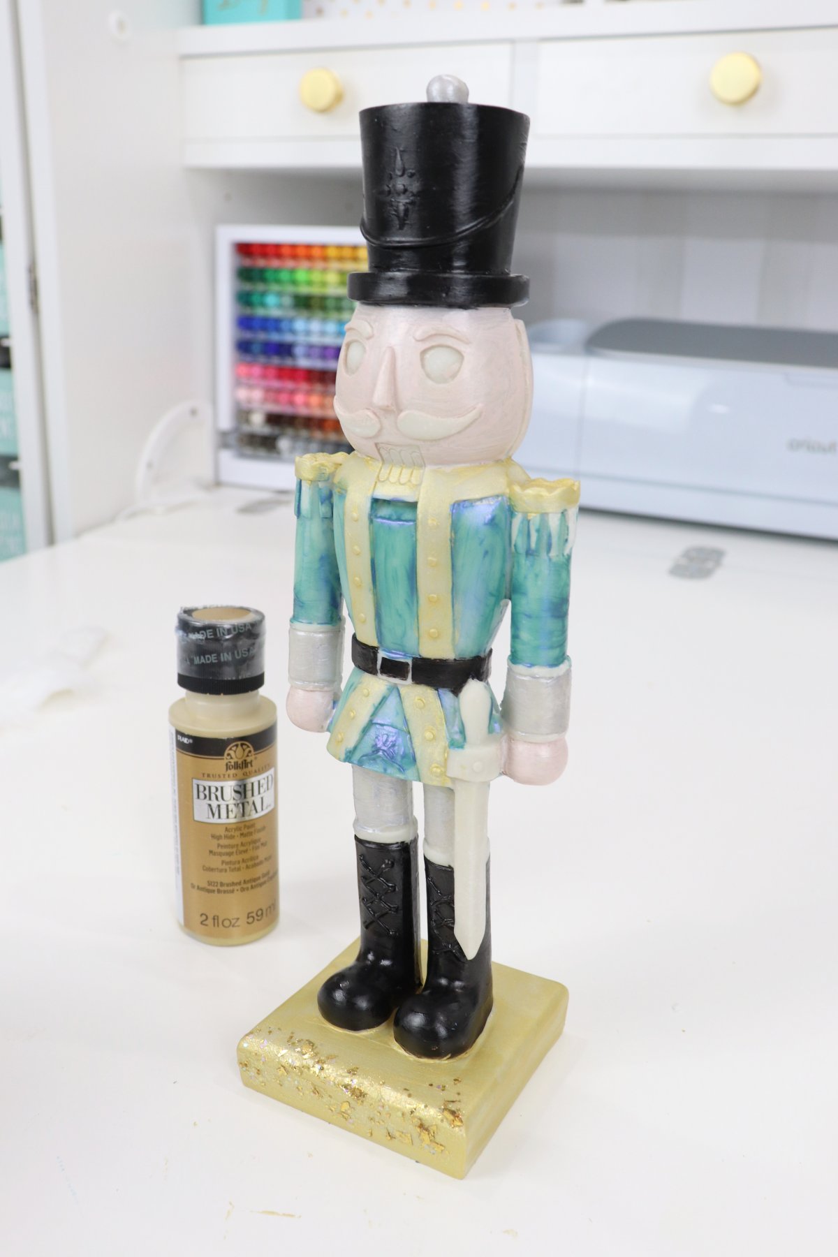 Image contains a partially painted nutcracker figurine with a bottle of gold paint beside it.