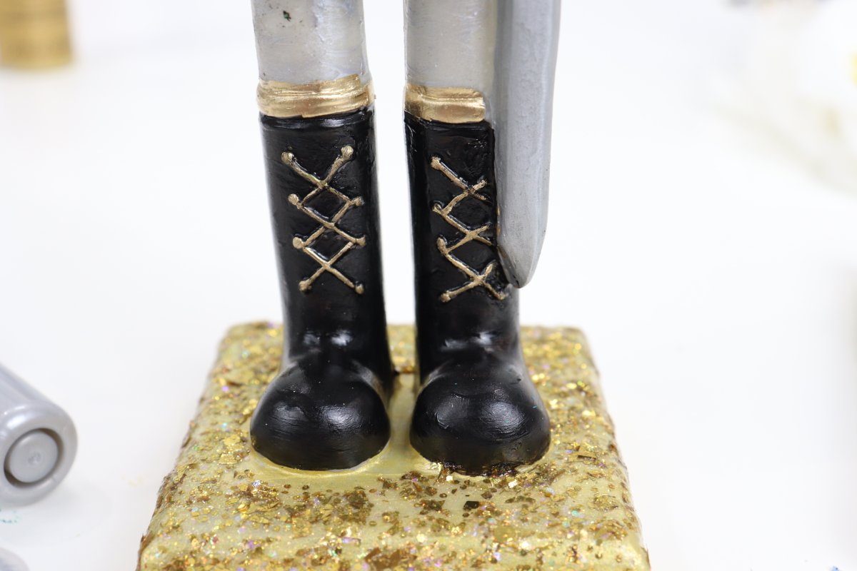 Image contains a closeup of the nutcracker figure's boots; black with gold laces on a glittered gold stand.