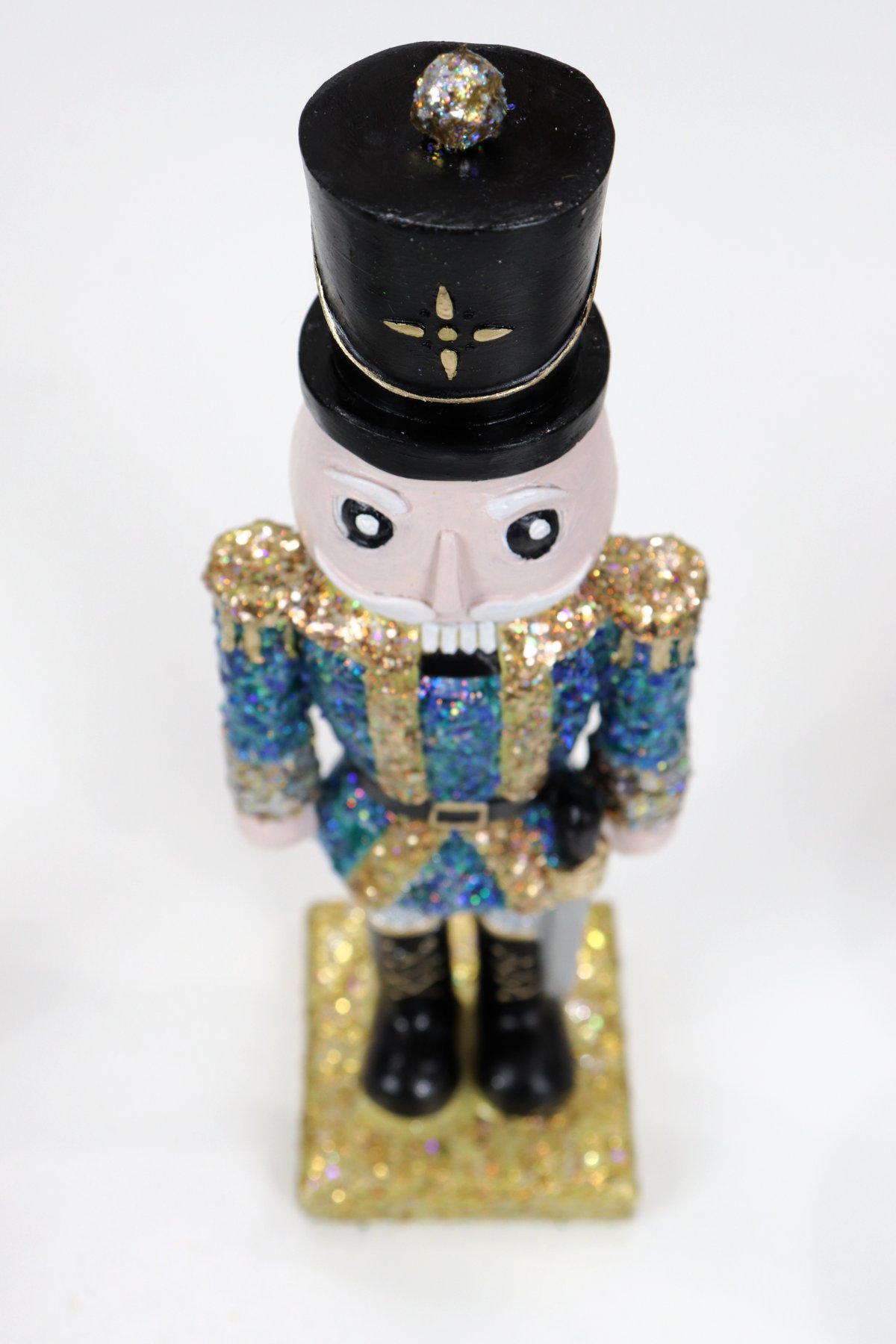 Image contains an overhead view of a hand-painted nutcracker figurine with a blue and gold jacket, gold stand, and black hat.