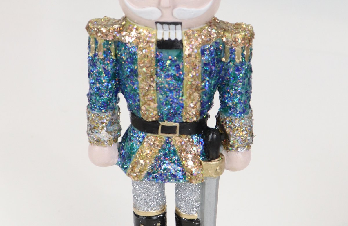 Image contains a close up view of a hand-painted nutcracker figure, specifically a blue and gold jacket, black belt, and silver pants.