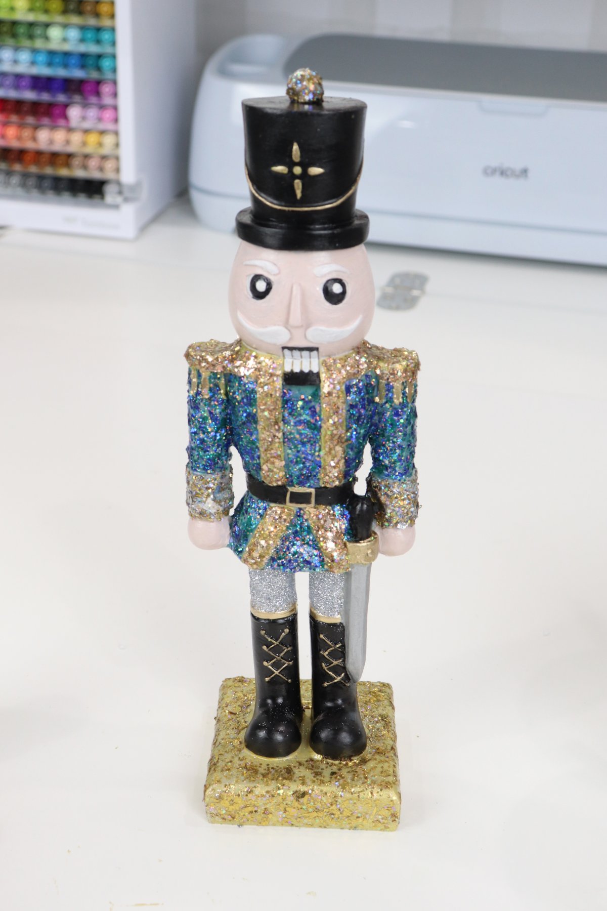 Image contains a handpainted Nutcracker figurine with a black hat and a glittered blue and gold jacket.