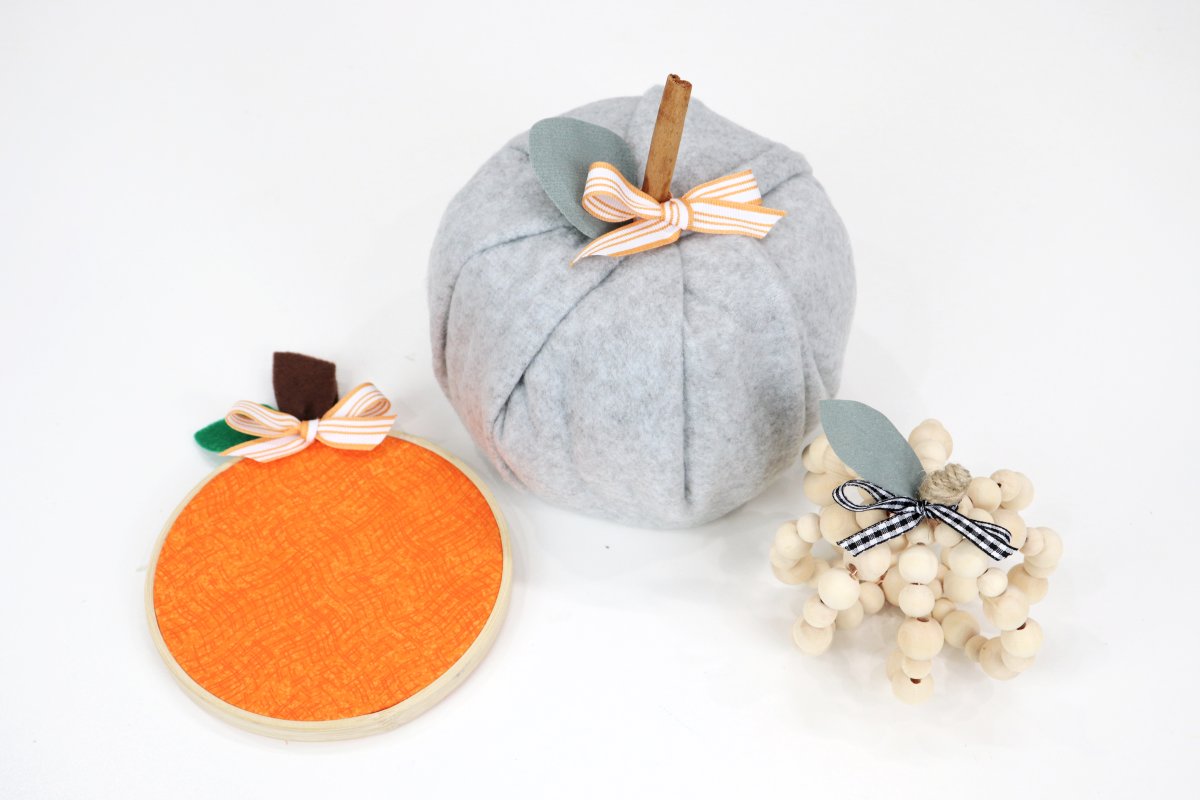 Image contains an embroidery hoop pumpkin, a toilet paper roll pumpkin, and a wooden bead pumpkin.