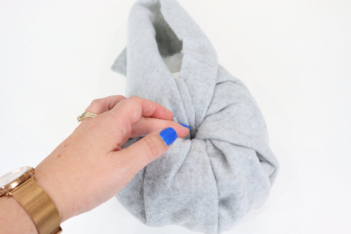 Image contains a woman's hand tucking grey fabric into the toilet paper roll tube.