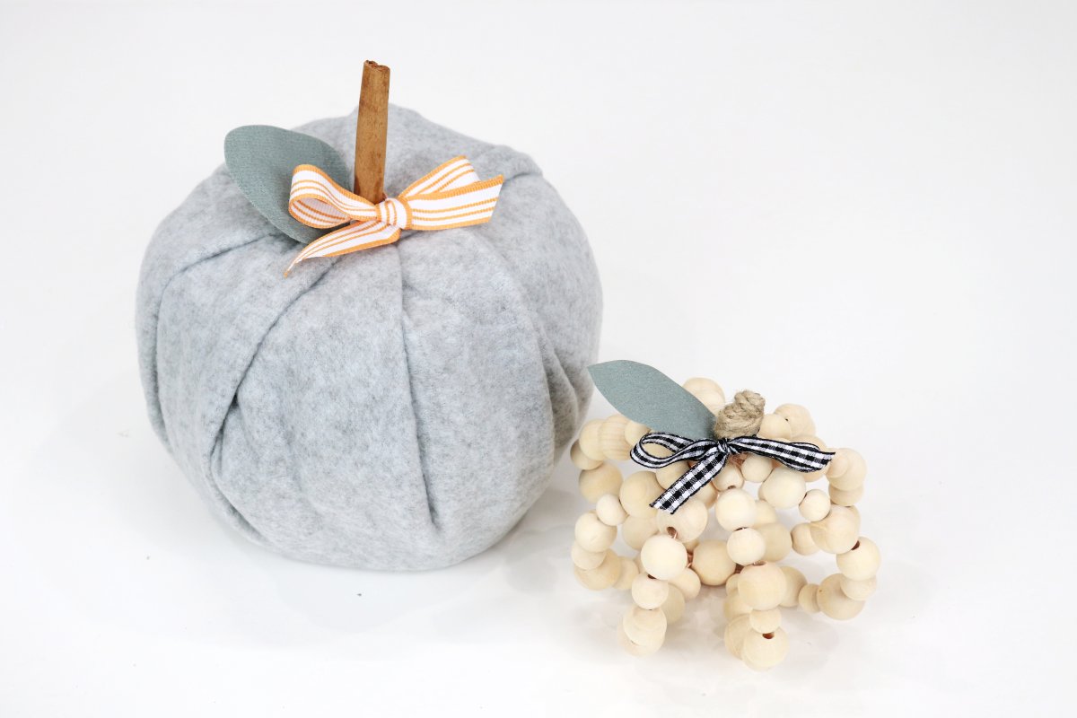 Image contains a grey fabric pumpkin and a smaller wooden bead pumpkin on a white background.