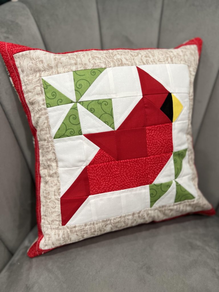 Image contains a quilted pillow with a red cardinal and green branches.