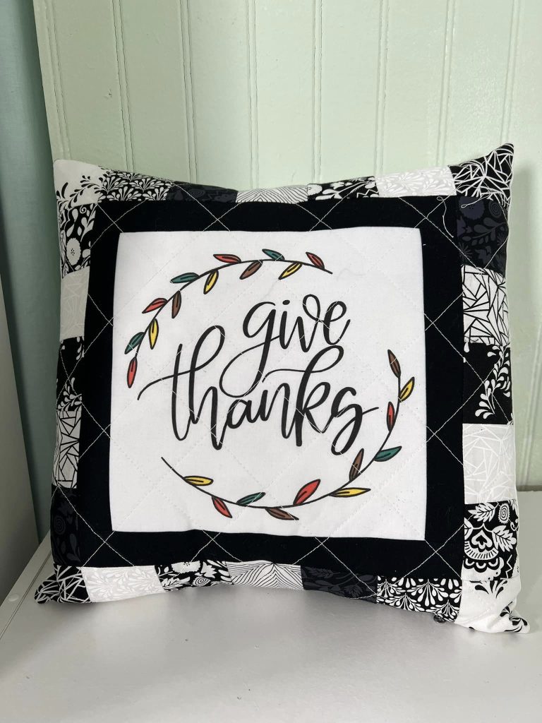 Image contains a black and white quilted pillow with the message, "give thanks."