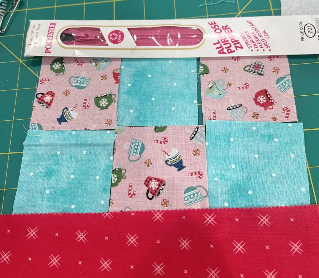Image contains blue, pink, and red fabric laid out in a patchwork pattern, and a pink zipper.