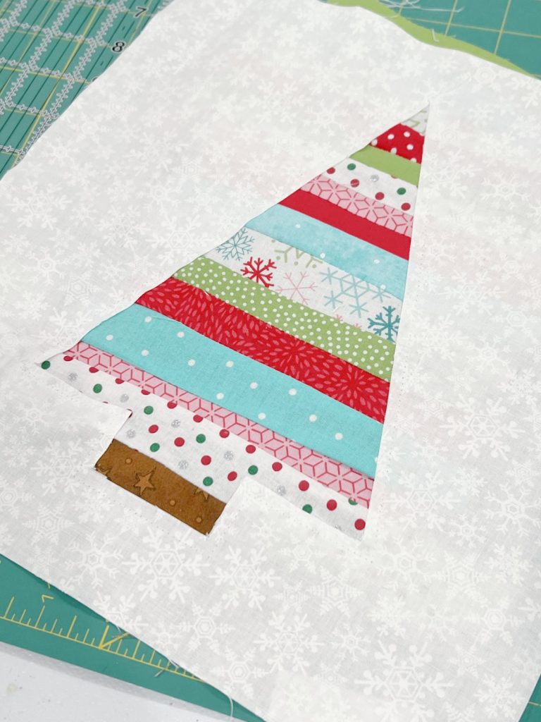 Image contains a white fabric square with a tree-shaped opening filled with colorful fabric stripes.