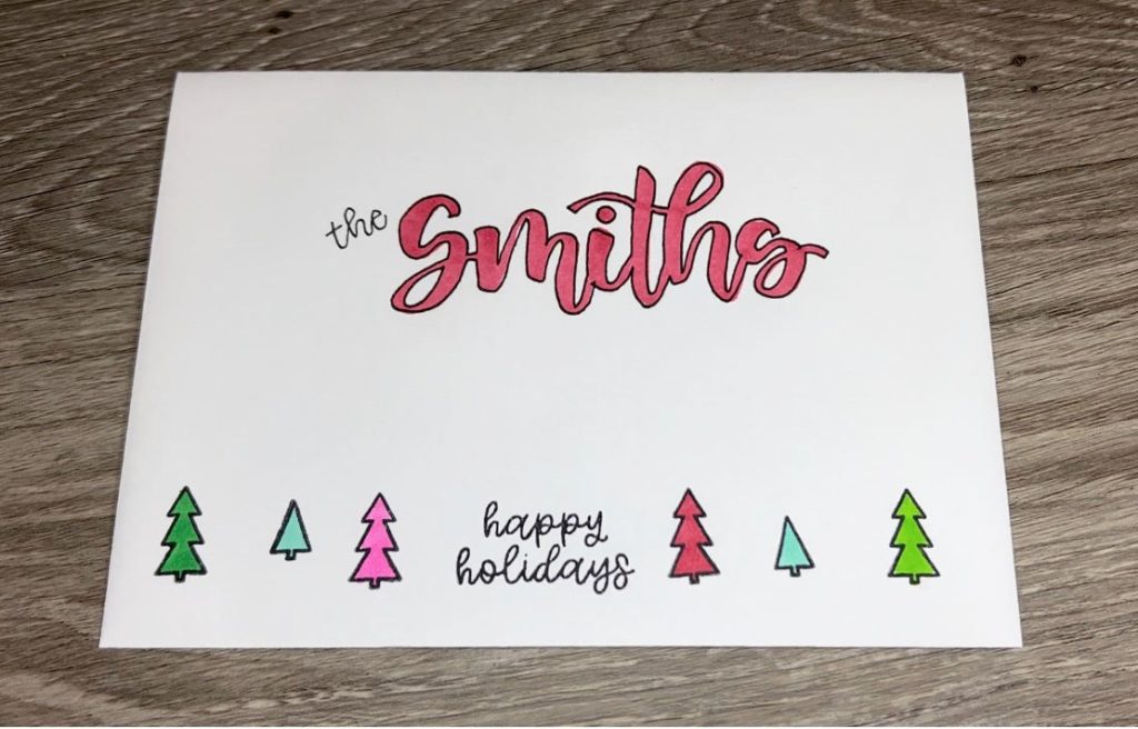 Image contains a white envelope decorated with green, teal, pink, and red trees stamped across the bottom, and "Smiths" written in red brush script in the center.