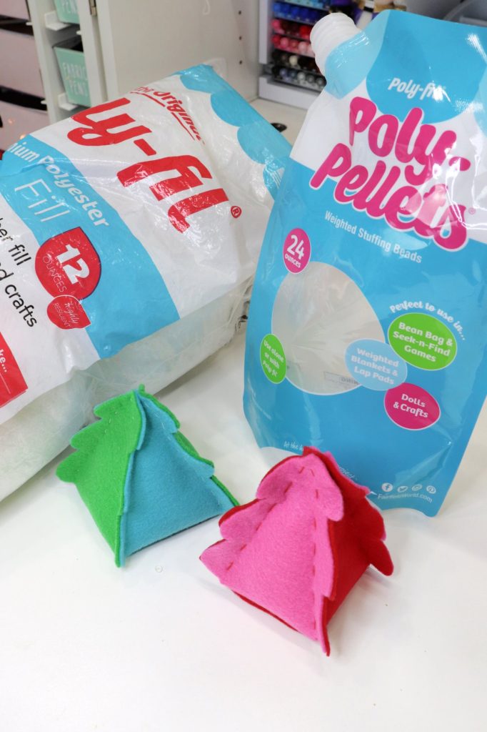 Image contains two felt Christmas trees in front of a bag of Poly-Pellets and a bag of Poly-fil.