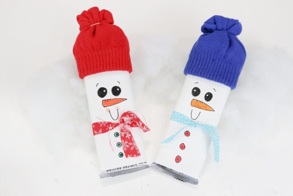 Image contains two snowmen made of candy bars wrapped in white paper and decorated with gloves for hats and fabric scrap scarves.