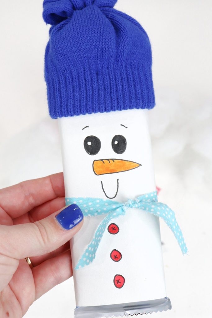 Image contains Amy's hand holding a snowman made of a wrapped candy bar with a blue glove hat.
