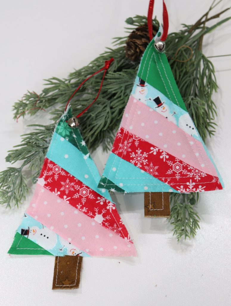 Image contains two tree shaped ornaments made from strips of leftover Christmas fabric, sitting on faux branches.
