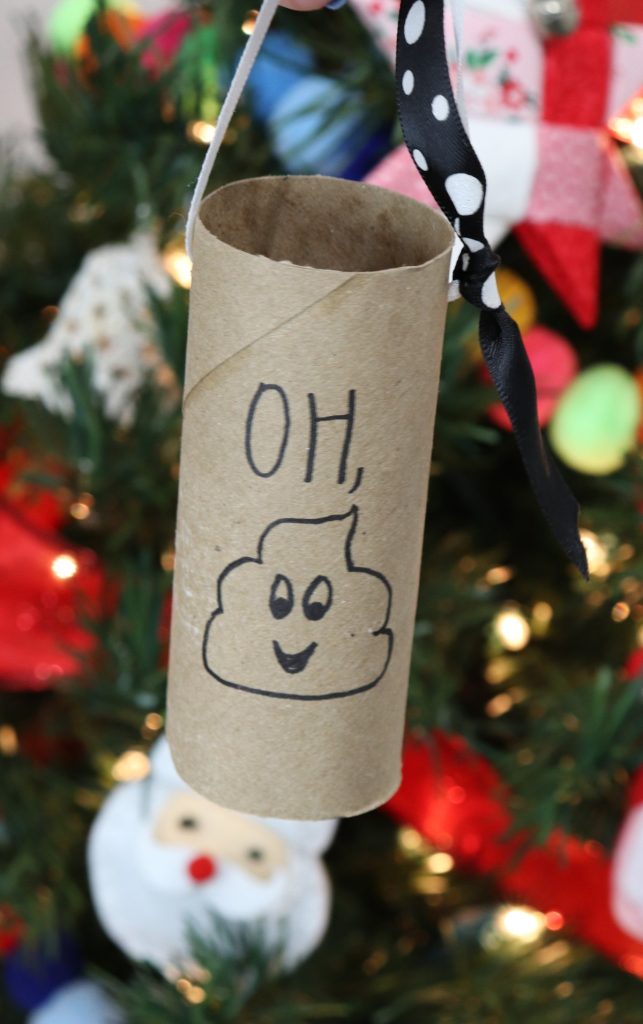 Image contains an empty toilet paper roll turned into an ornament with a black and white ribbon and, "oh, poop" drawn on the side. It hangs on a decorated tree.