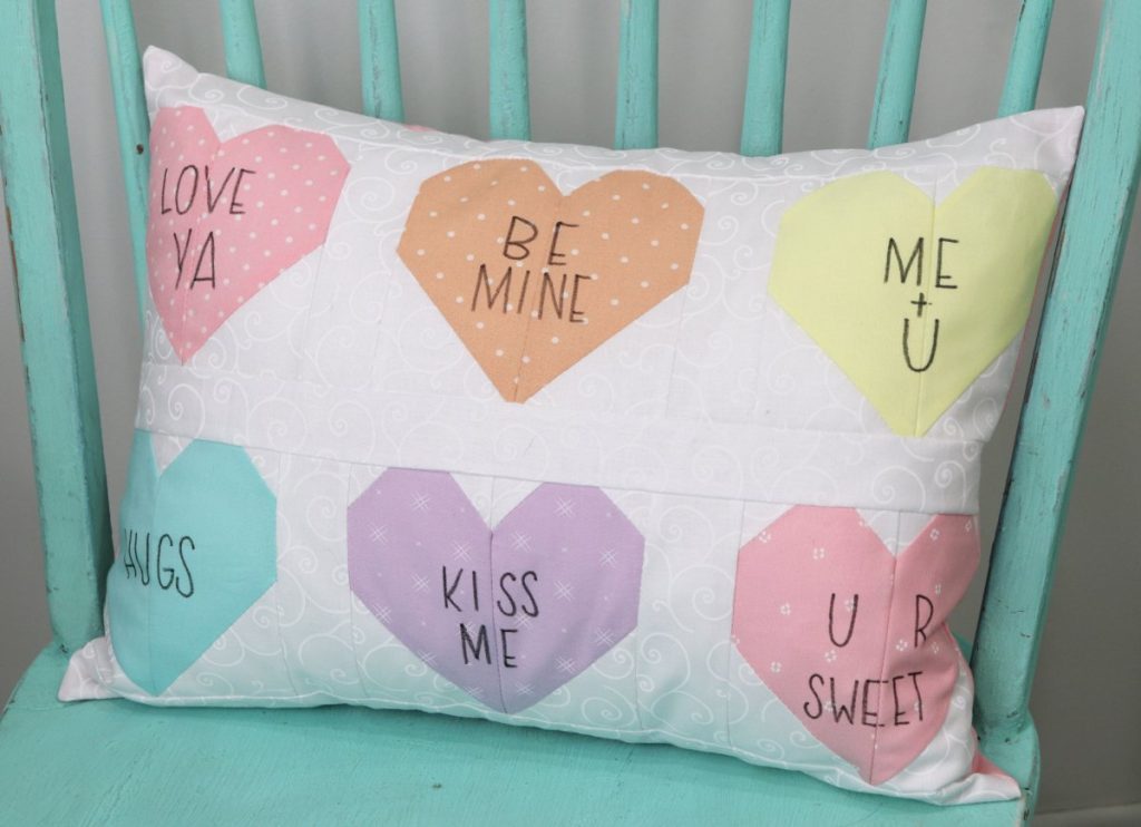 Image contains a rectangular white pillow with six colored fabric hearts, each with a message written in black marker.