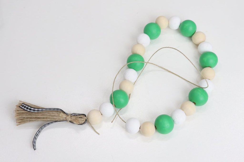 Image contains green, white, and natural wooden beads strung on a piece of jute with a jute tassel on one end.