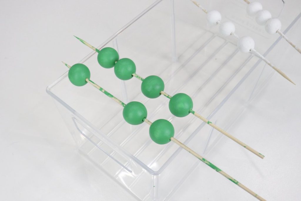Image contains green and white painted wooden beads on wooden skewers.