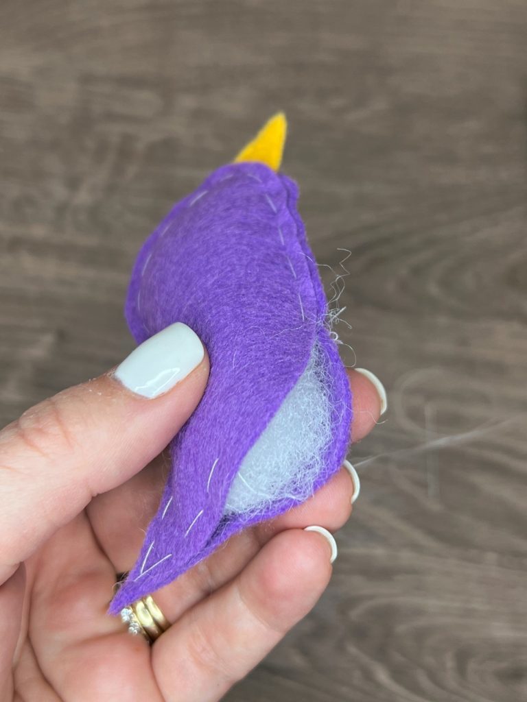 Image contains Amy's hand holding the felt bird with the bottom opening visible and filled with Poly-Fil.