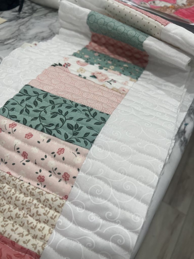 Image contains a table runner that has been quilted with wavy vertical lines.