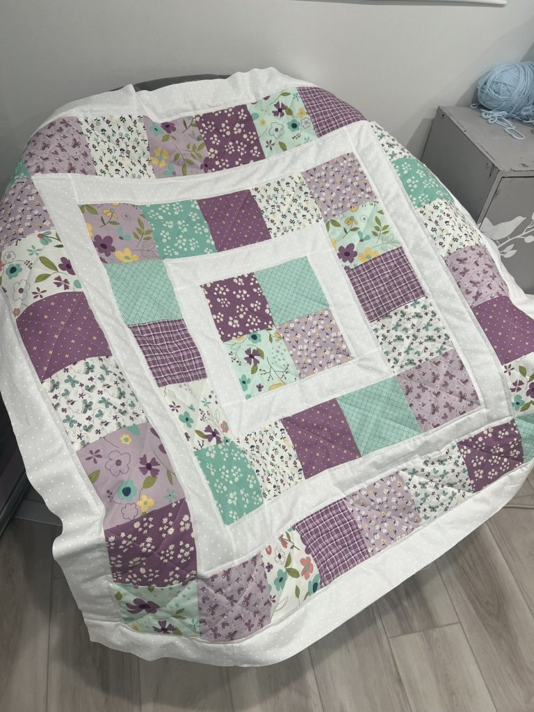 Image contains a partially finished quilt made from white, teal, and purple fabric squares.