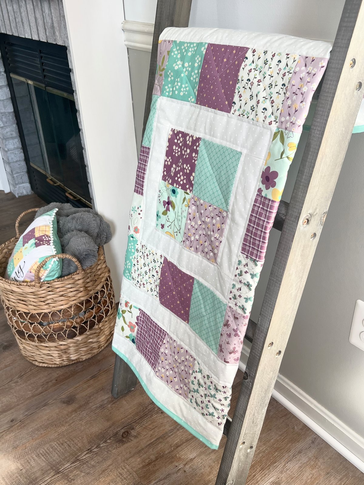 Image contains a purple and teal quilt hanging on a wooden ladder.
