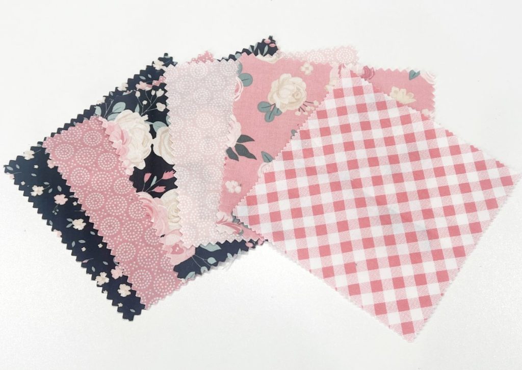 Image contains six 5” fabric squares. The squares are a variety of patterns with black, pink, green, and white flowers, swirls, and plaid.
