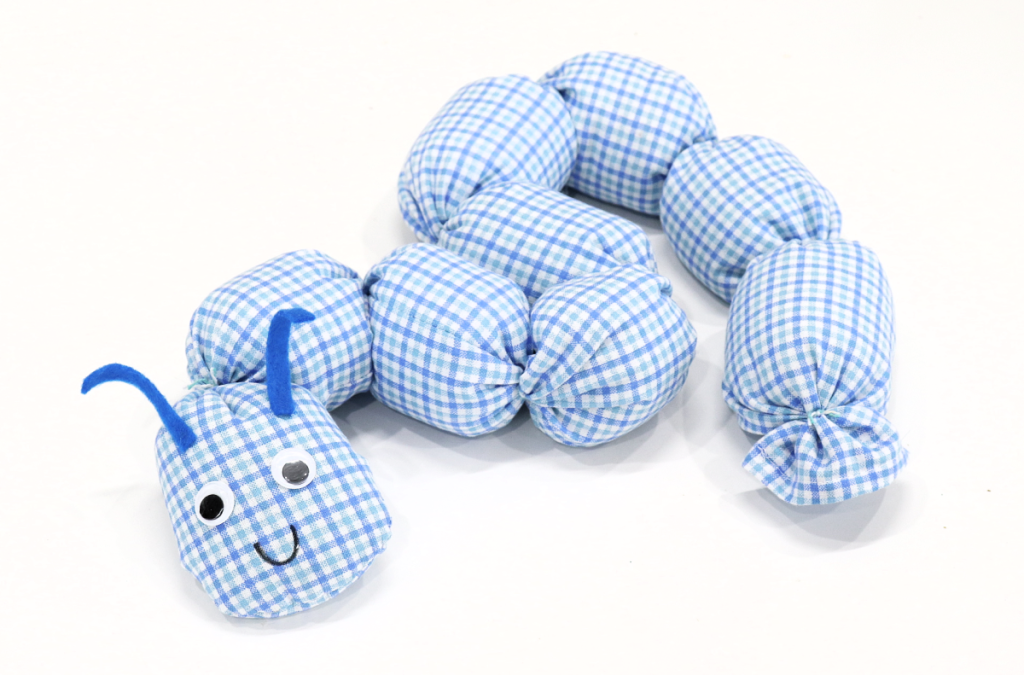 Image contains a plush caterpillar made from blue and white plaid fabric, on a white background.