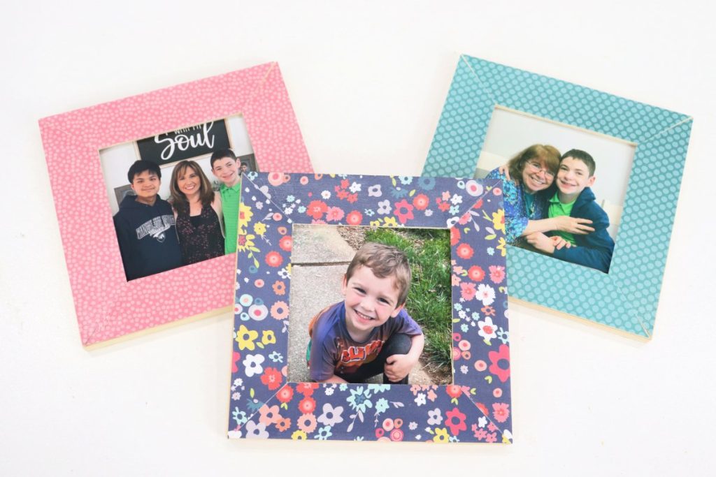 Image contains three square photo frames that have been decoupaged with scrapbook paper. One has pink paper with small lighter pink dots, one has teal polka dot paper, and one has dark blue paper with multicolored flowers.