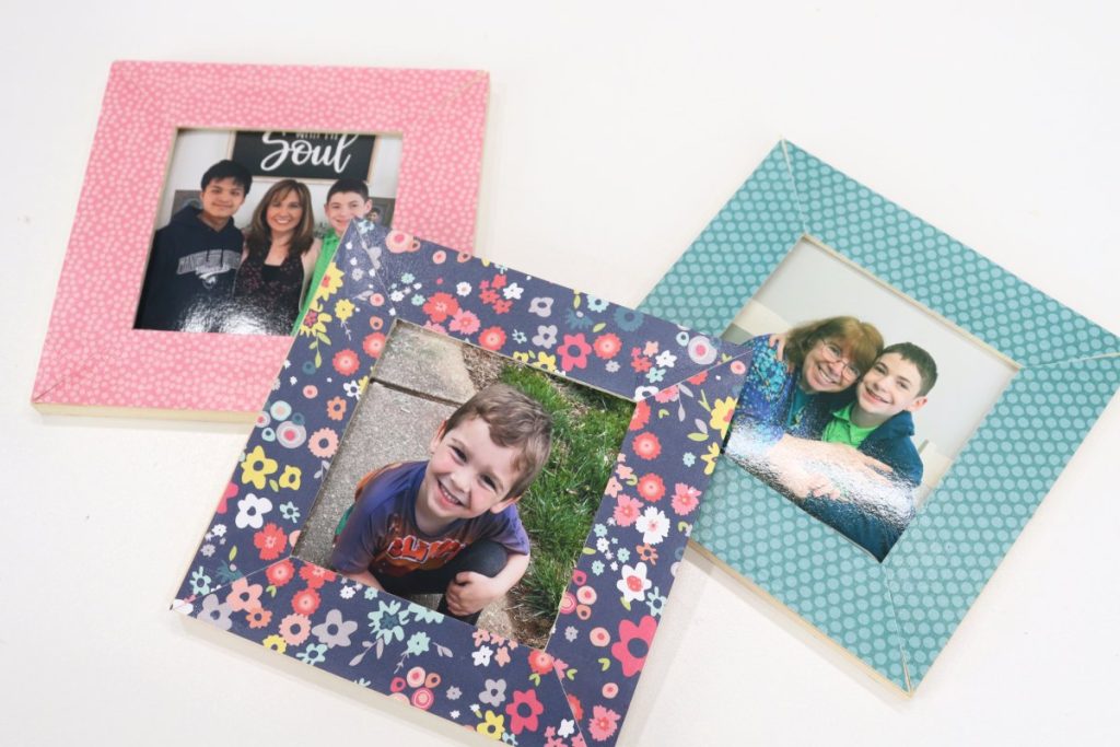 Image contains three decoupaged photo frames; one pink, one teal, and one blue with multicolored flowers.