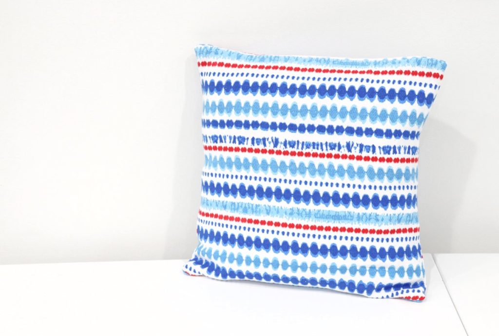 Image contains a square pillow with a red, white and blue striped pillow cover.
