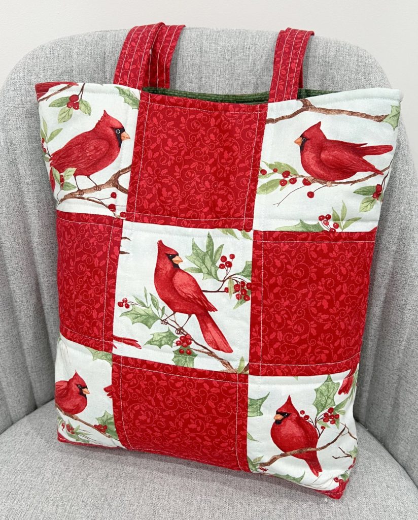 Image contains a fabric tote bag made of red and cardinal print patchwork blocks.