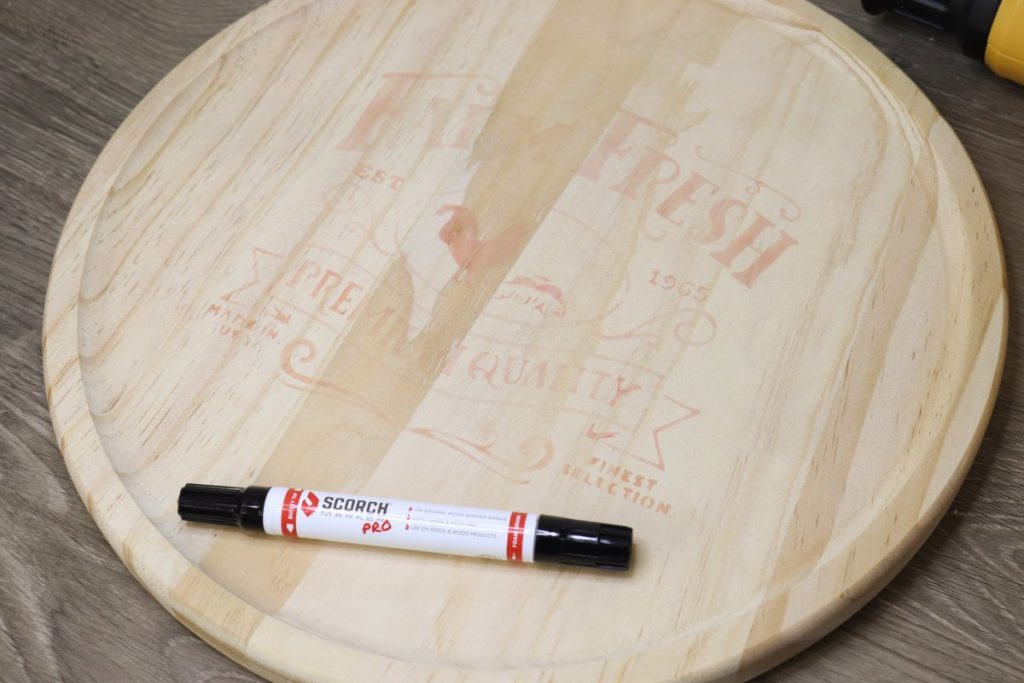 Image contains a round wooden tray with a design stenciled onto it in a light pink ink. A Scorch Marker sits on top of the tray.
