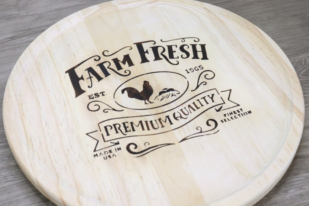 Image contains a round wooden tray with a “farm fresh” farmhouse design wood burned onto the center.