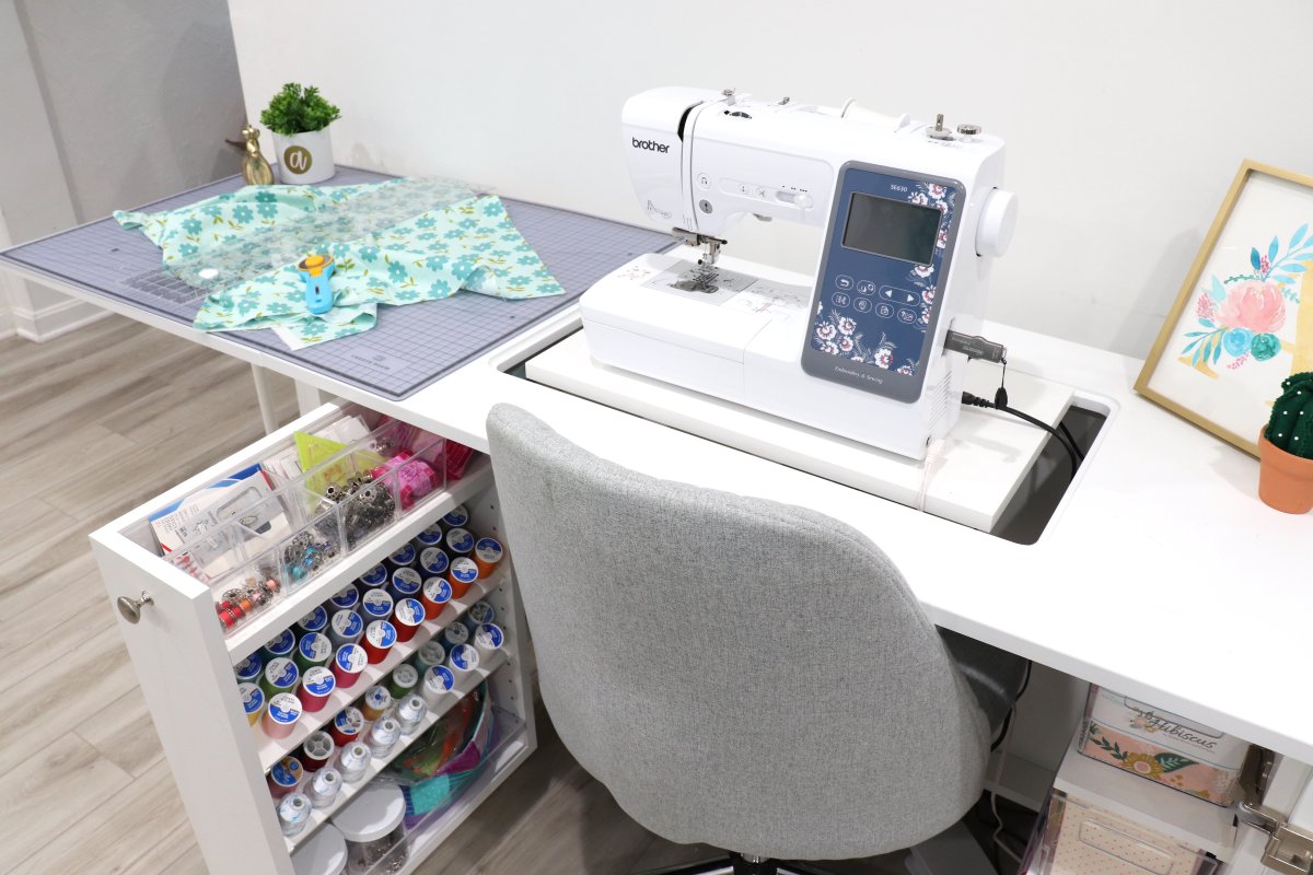 Image contains the Create Room Sew Station with a sewing machine on top and a grey plush chair.