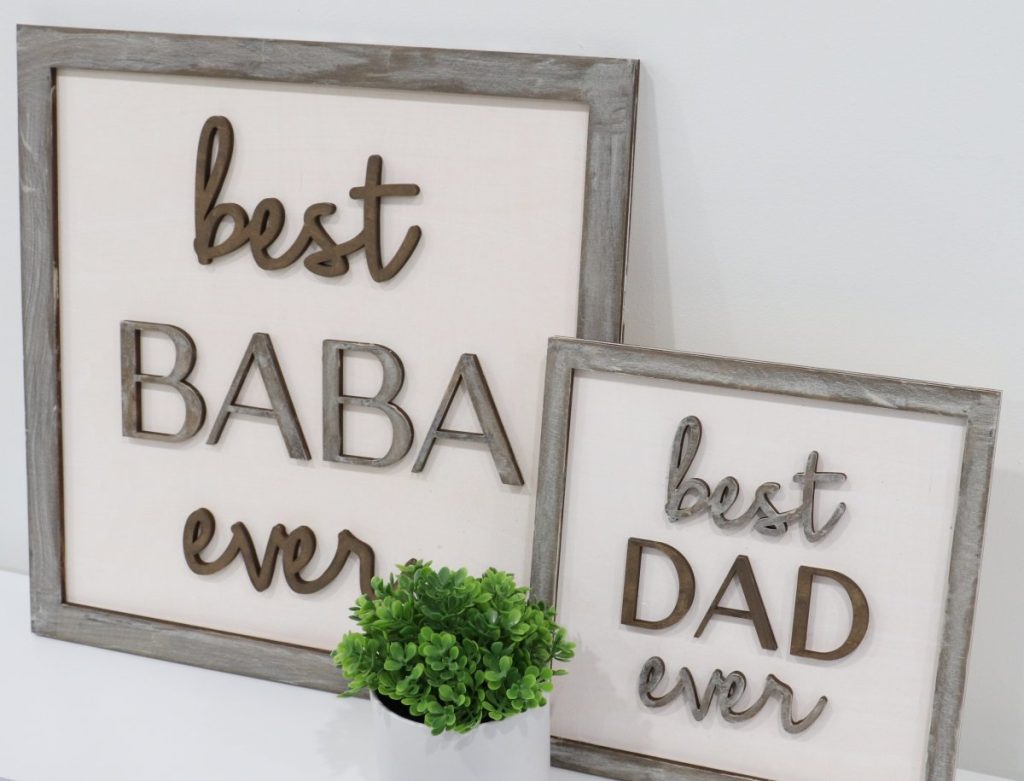 Image contains two wooden signs; one with the words “best baba ever,” and one with the words, “best dad ever.” A faux plant sits in between.