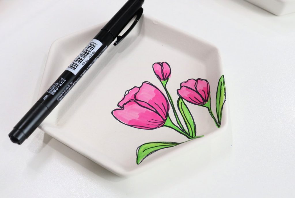 Image contains a white jewelry tray with three pink tulips drawn on it, and a black permanent marker sitting on top.