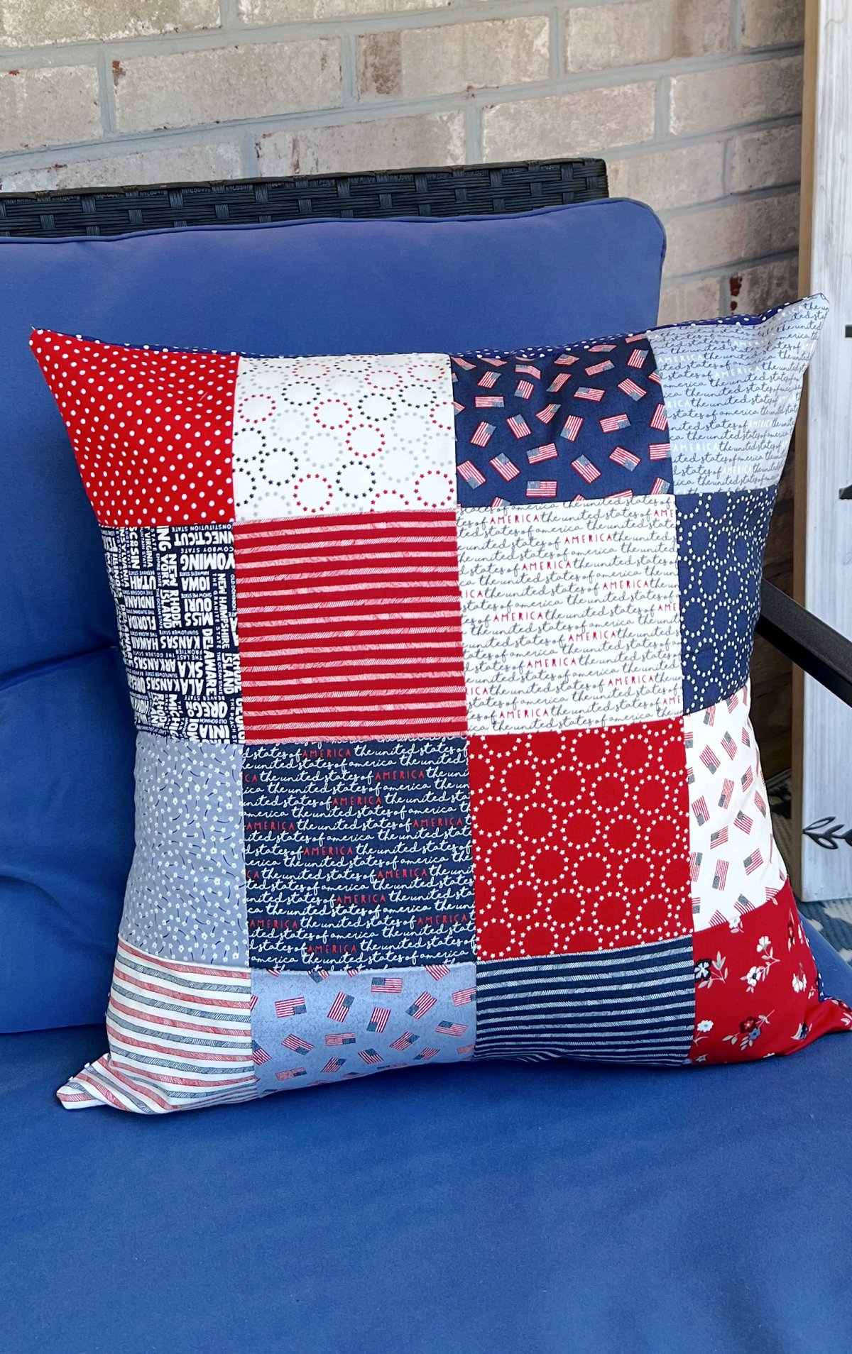 Image contains a square patchwork pillow made of red, white, and blue fabric sitting on a blue outdoor chair.