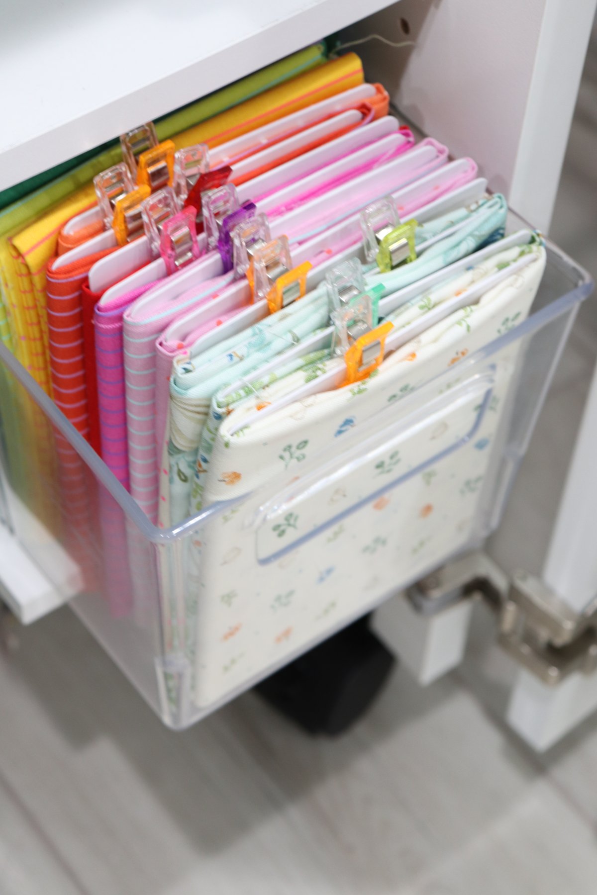 Image contains multicolored fabric fat quarters organized in a clear plastic tote.