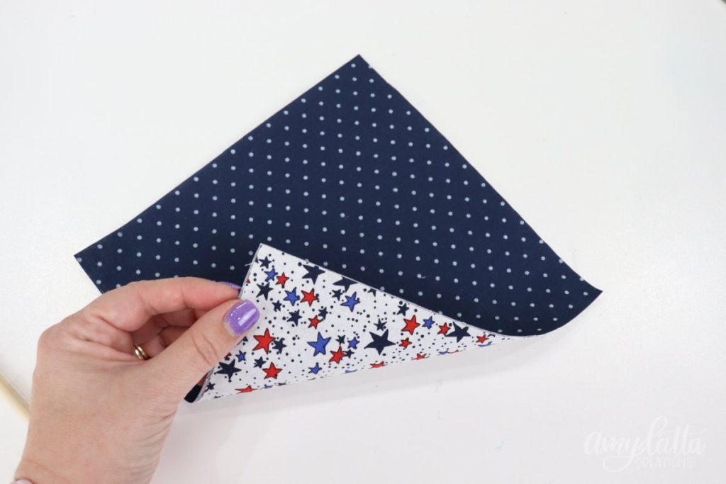 Image contains Amy’s hand holding a double sided fabric square; the top side is navy with white dots, the bottom is white with red and blue stars.