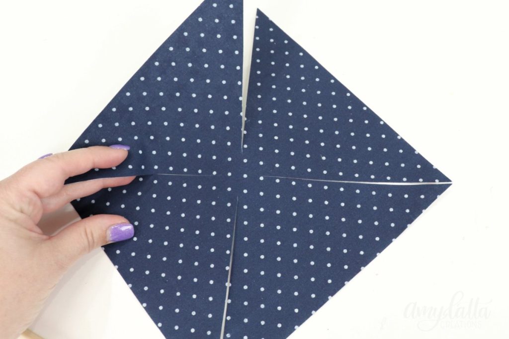 Image contains Amy’s hand holding a fabric square that has been cut in toward the center from each of the four corners.