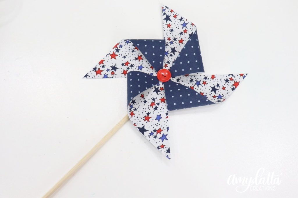 Image contains a blue and white fabric pinwheel on a wooden dowel with a red button in the center.