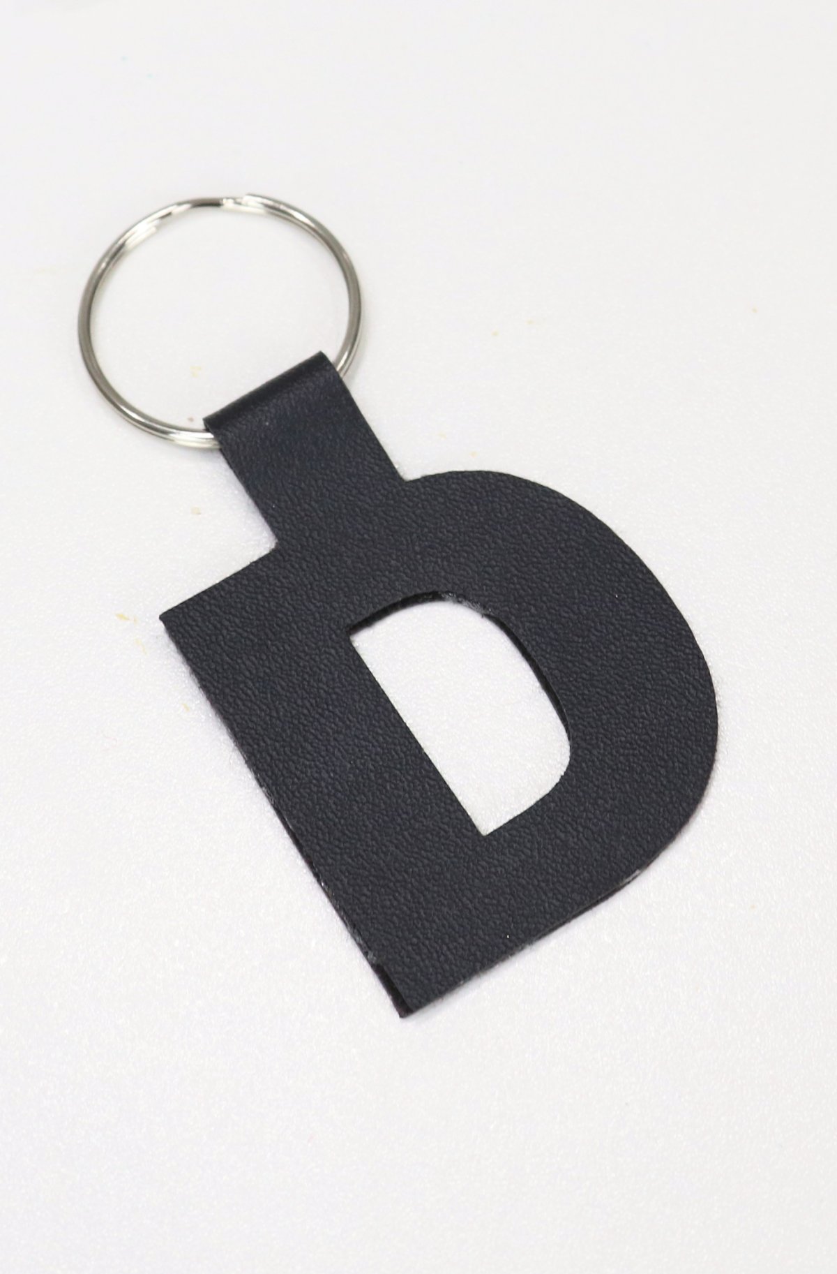 Image contains a black monogram “D” cut from faux leather and attached to a metal keyring.
