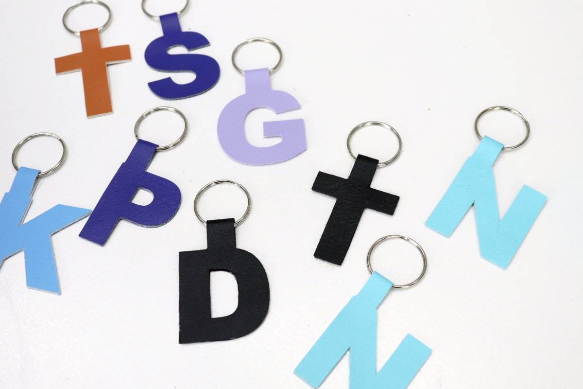 Image contains a variety of faux leather monogram keychains in assorted colors on a white table.