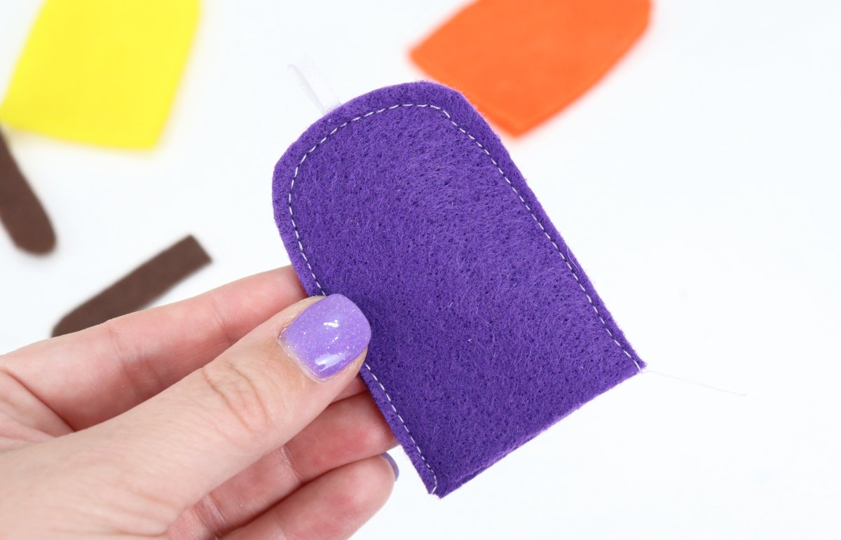 Image contains Amy’s hand holding the top of the purple felt popsicle.