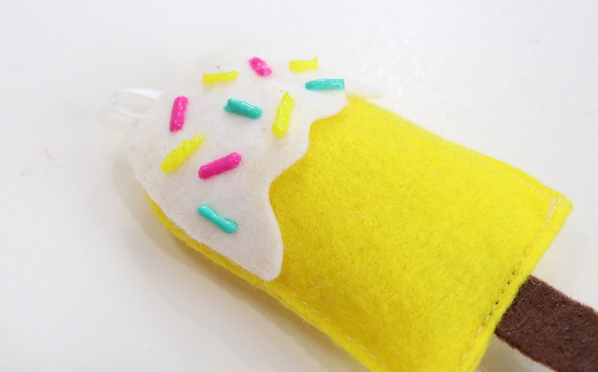 Image contains a yellow felt popsicle with colorful fabric paint sprinkles.