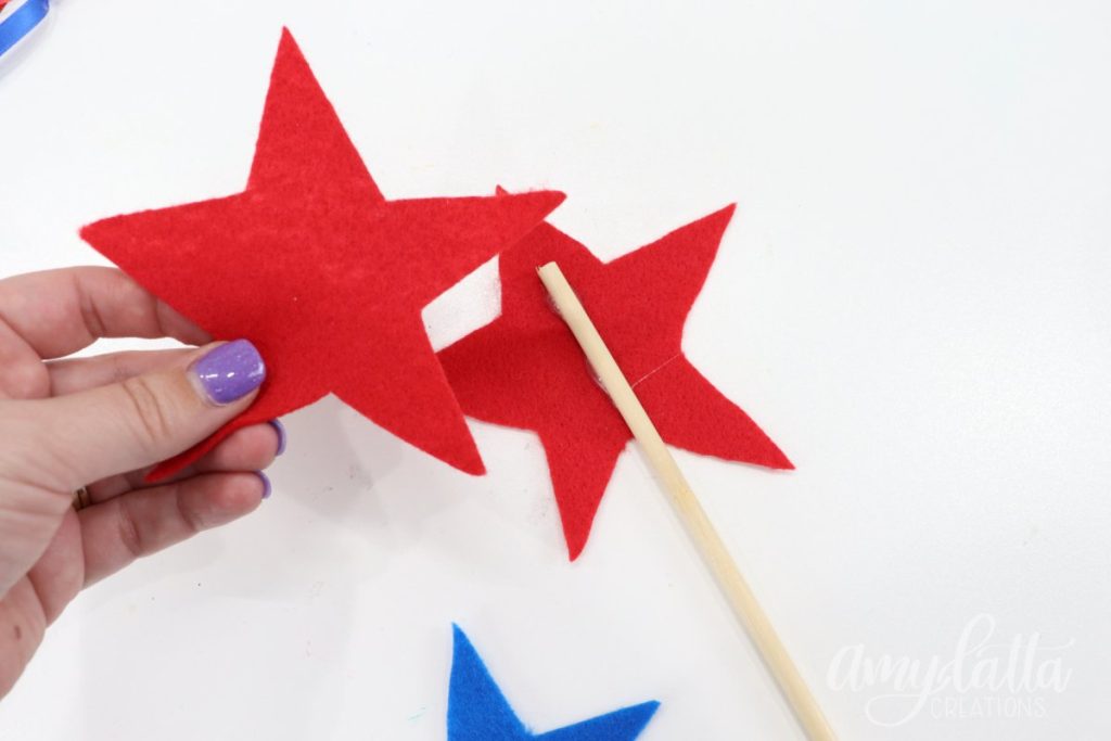 Image contains a red felt star with a wooden dowel on top, and Amy’s hand holding a second red felt star.