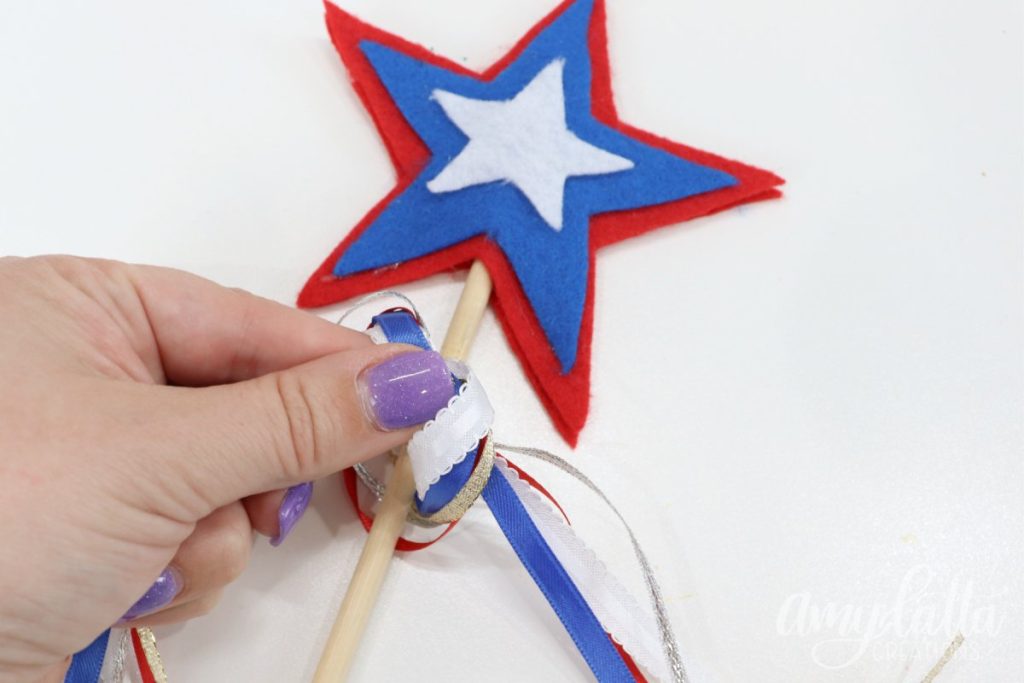 Image contains Amy’s hand tying assorted red, white, and blue ribbons onto a wooden dowel with a felt star topper.