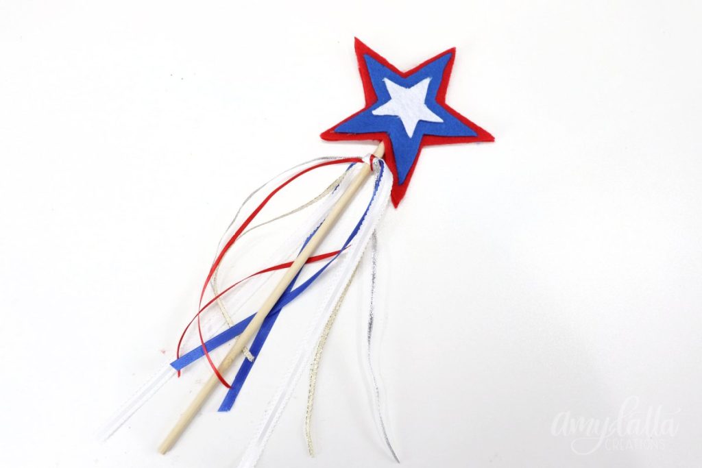 Image contains a wooden dowel with a red, white, and blue felt star topper and ribbon streamers.
