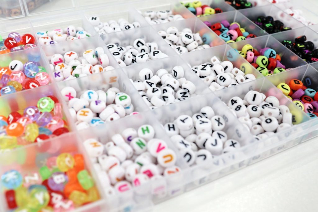 Image contains a divided plastic tray containing beads with letters and numbers on them.